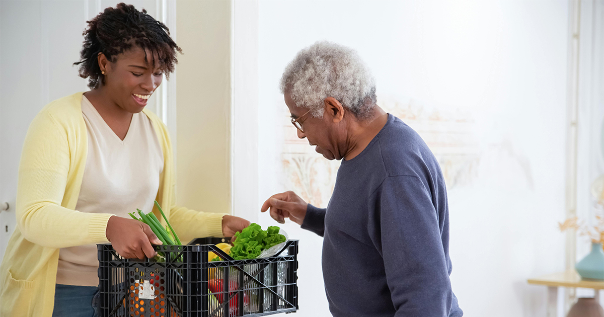 Woman holds a plastic delivery of prescription produce for an older man Woman holds a plastic delivery of prescription produce for an older man