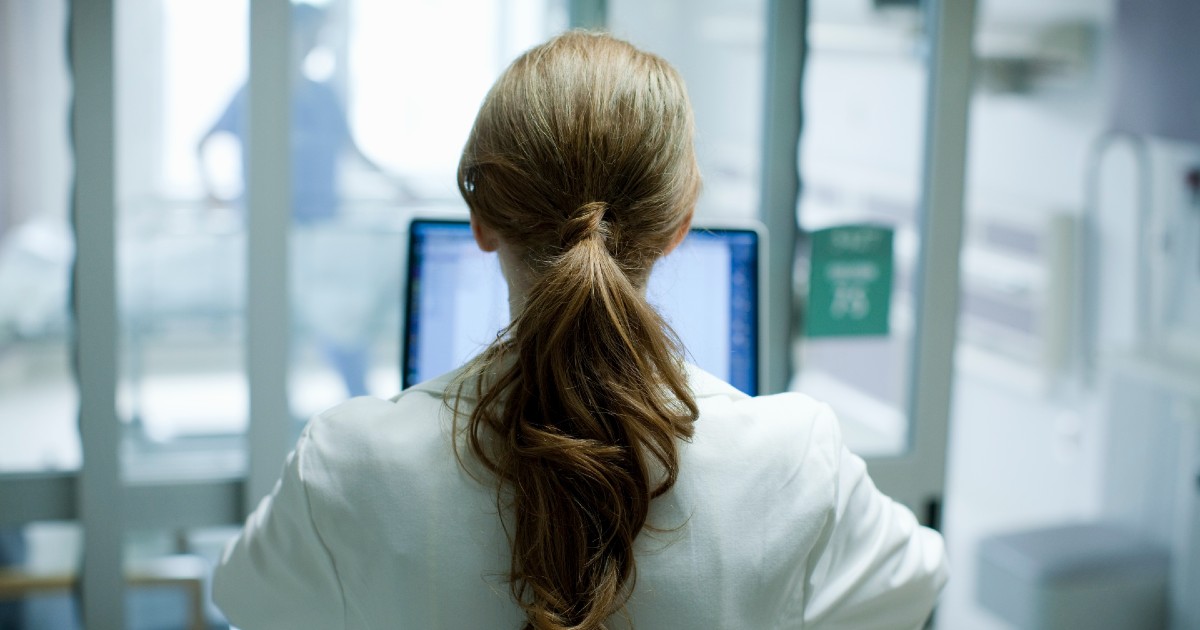 Doctor with long hair in a ponytail sits and works on a laptop Doctor with long hair in a ponytail sits and works on a laptop