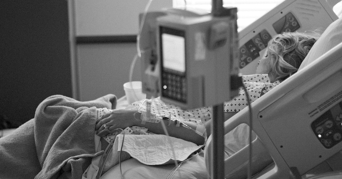 Woman asleep in hospital bed with IV in foreground Woman asleep in hospital bed with IV in foreground