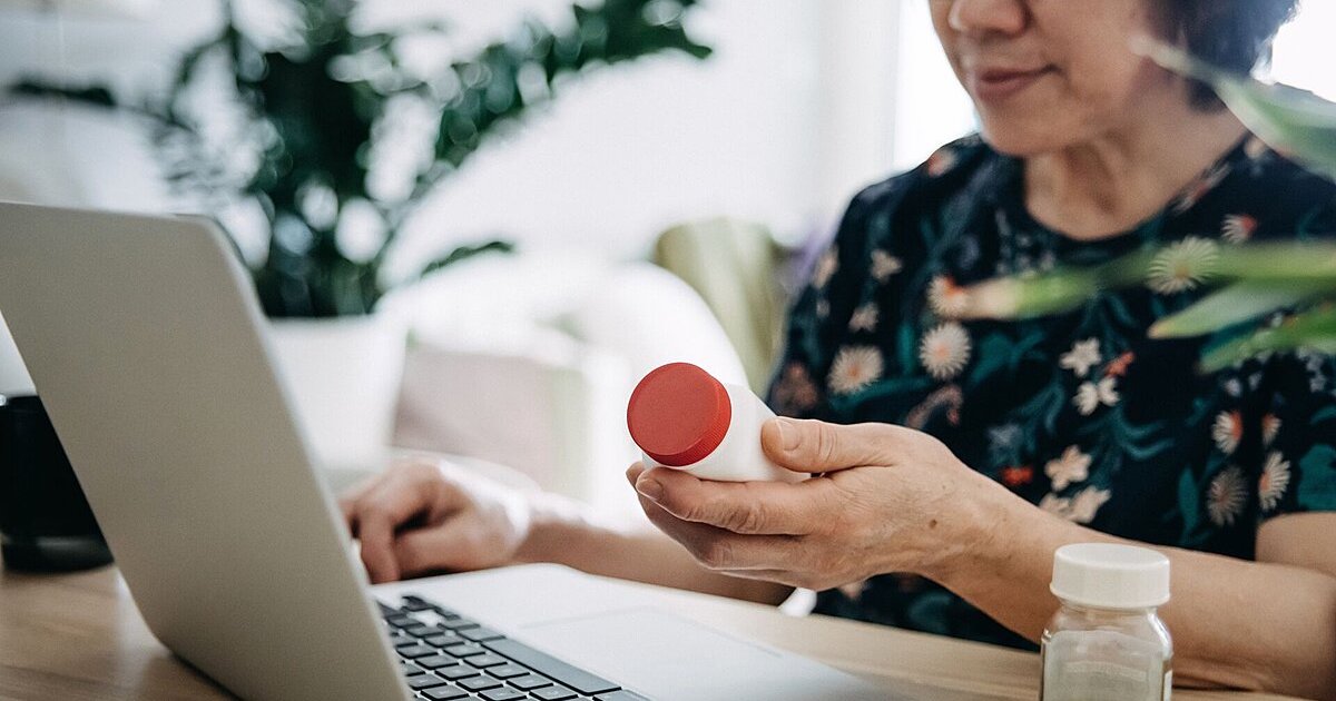 Patient checks pill bottle against her patient record on a laptop Patient checks pill bottle against her patient record on a laptop