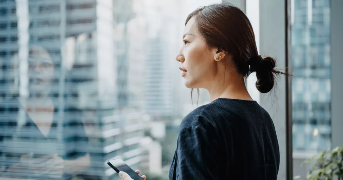 A person holding a smartphone staring outside the office window A person holding a smartphone staring outside the office window
