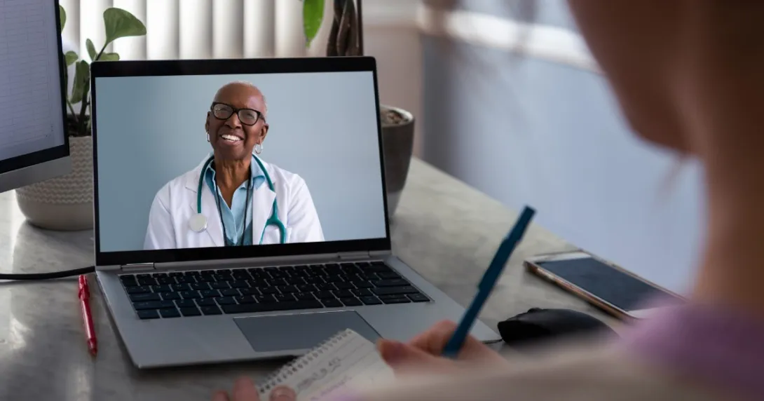 Female doctor on laptop smiles at patient in foreground who is taking notes Female doctor on laptop smiles at patient in foreground who is taking notes